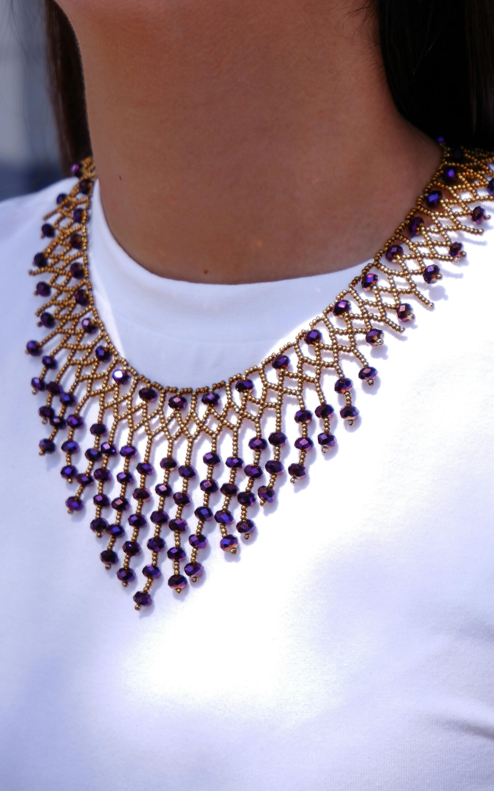 Close-up of a stylish purple and gold beaded necklace showcased on white fabric, perfect for fashion and accessory themes.